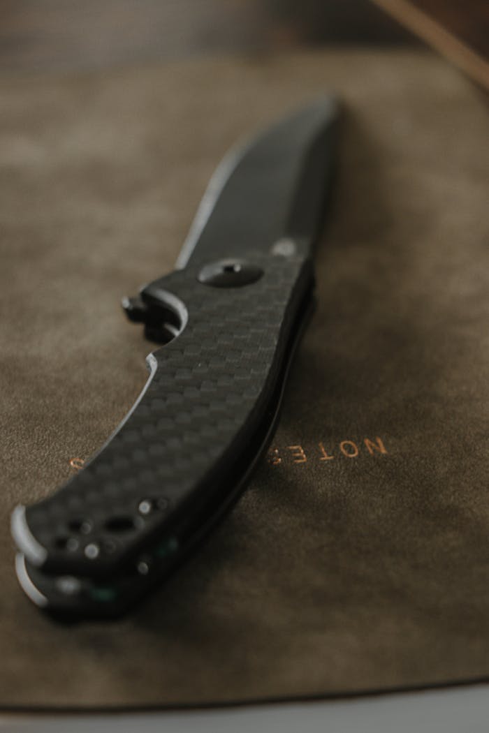 Close-up of a tactical folding knife on a leather surface, showcasing its design and sharpness in a still life setting.