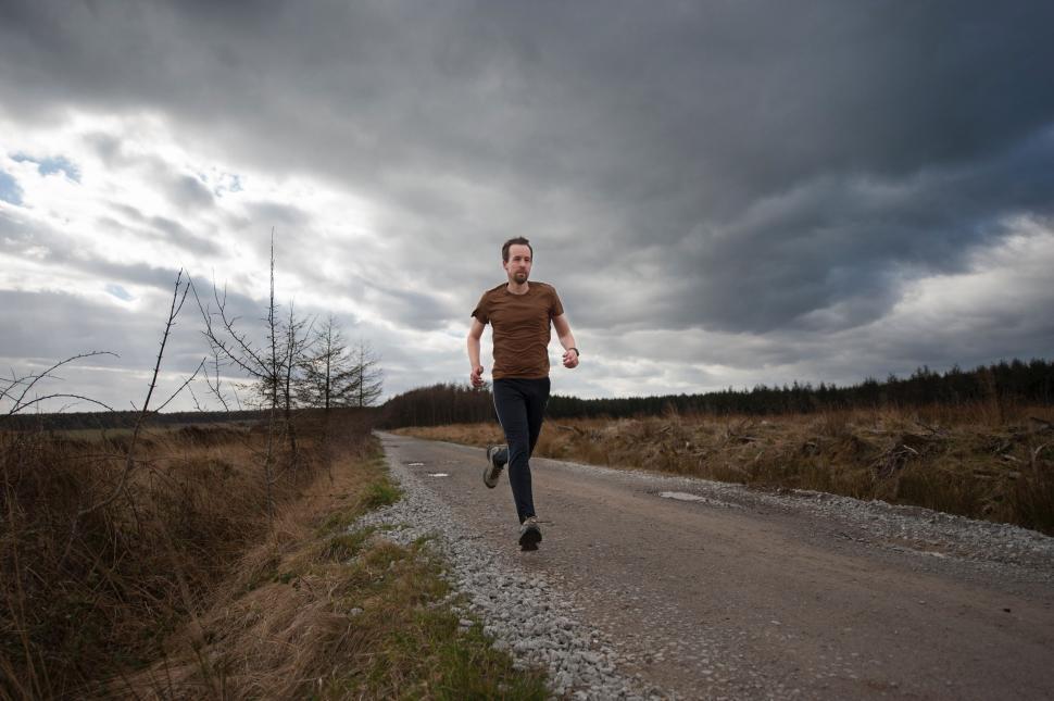 man running down dirt road under cloudy sky